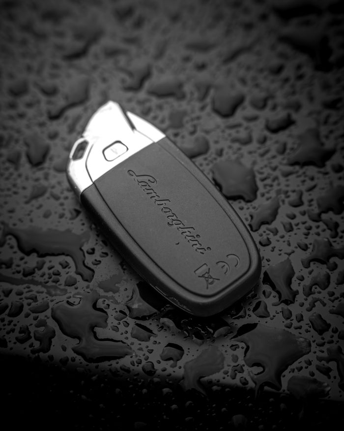 Close-up of a luxury car key on a wet, textured surface, highlighting elegance and style.